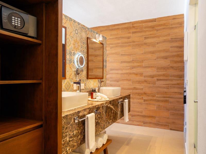 Světelná koupelna s dřevěnými a mramorovými detaily a malým trezorem na polici.