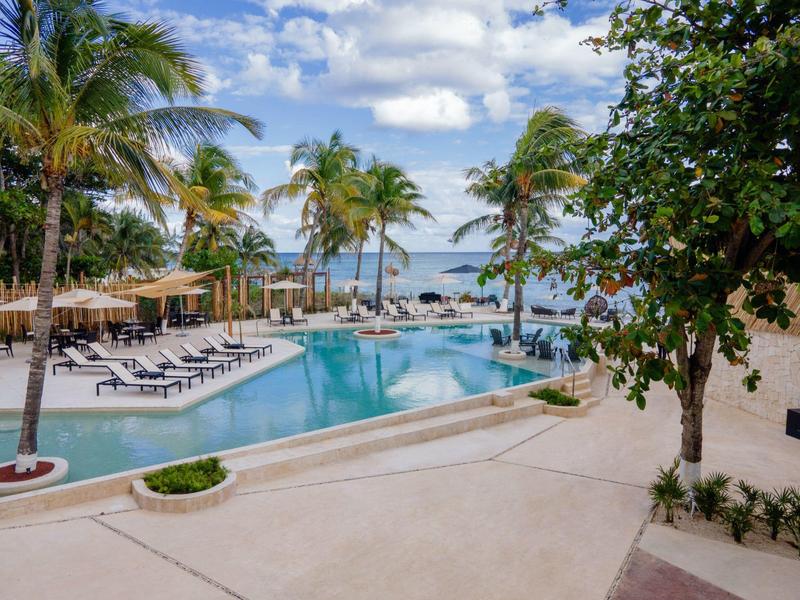 Velký bazén s lehátky pod palmami v slunném hotelu na pláži.