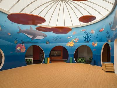 Area interna per bambini con murale a tema oceano e sedute sotto una cupola.