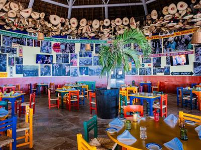 Ristorante colorato con cappelli appesi, sedie colorate e una pianta al centro.