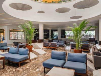 Hall d'hotel moderno con poltrone blu, piante e luce tonda a soffitto.