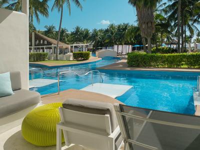 Area salotto moderna con vista su piscina e palme in un resort tropicale.