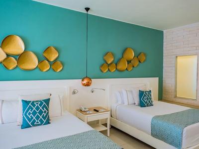 Camera d'hotel con due letti matrimoniali, accenti murali turchesi e decorazioni murali dorate.