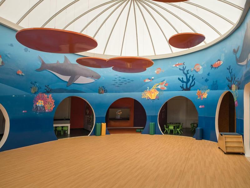 Area interna per bambini con murale a tema oceano e sedute sotto una cupola.
