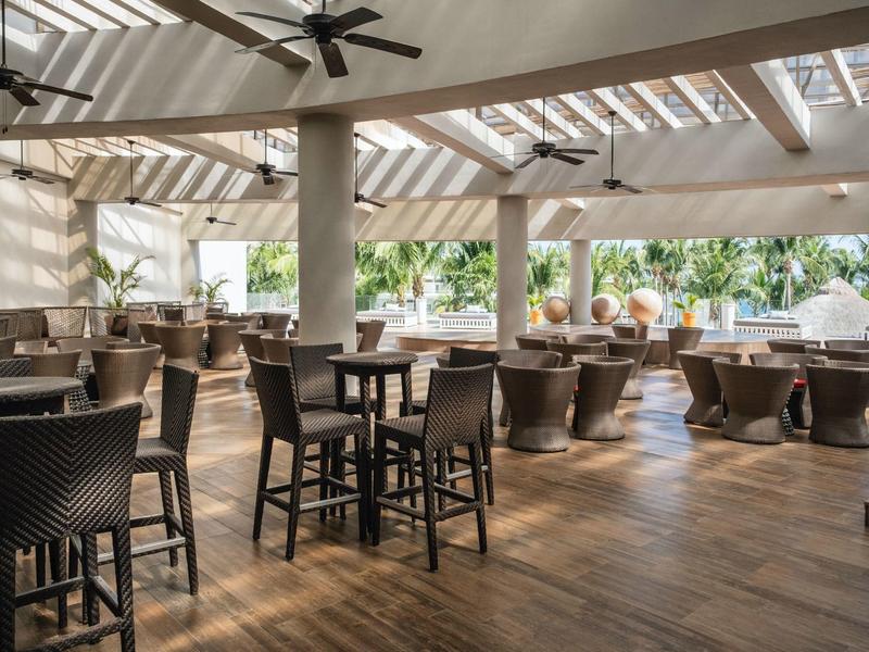 Ristorante luminoso e arioso con pavimento in legno e mobili scuri sotto i ventilatori a soffitto