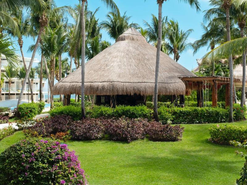 Palme circondano una capanna tradizionale di paglia in un resort tropicale con prati curati e piante.