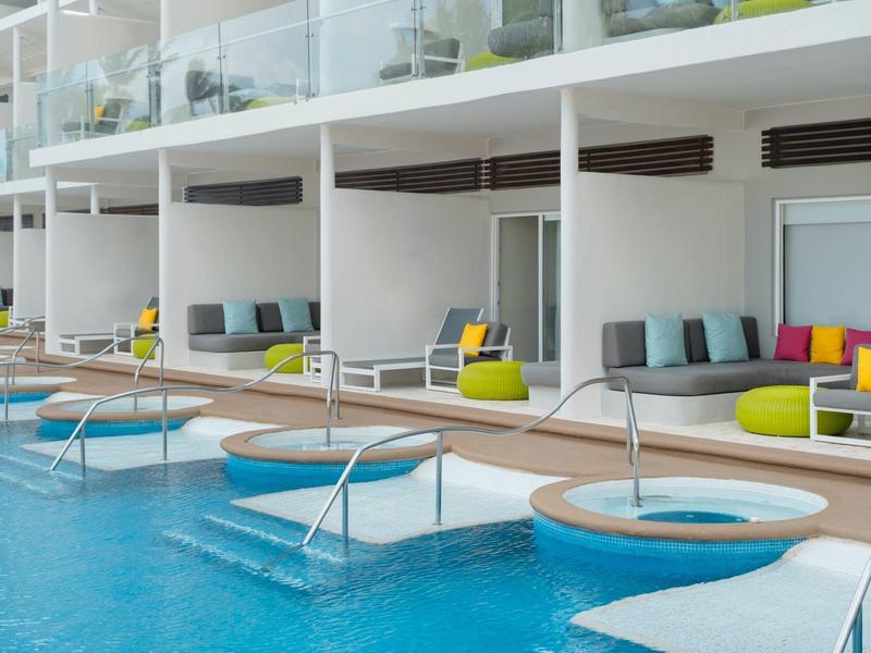 Piscina moderna dell'hotel con aree salotto, cuscini colorati e jacuzzi ai bordi della piscina.