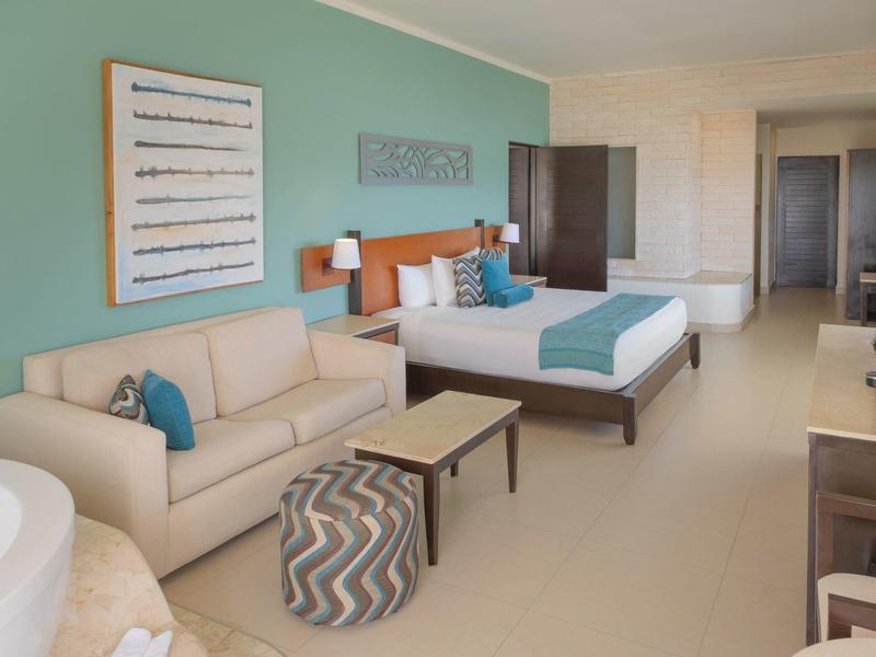 Camera d'hotel moderna con letto, divano e accenti decorativi in colori chiari.