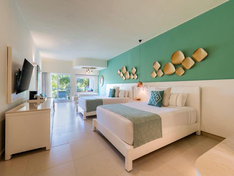 Camera d'hotel moderna con due letti, accento verde sulla parete e vista sul balcone.