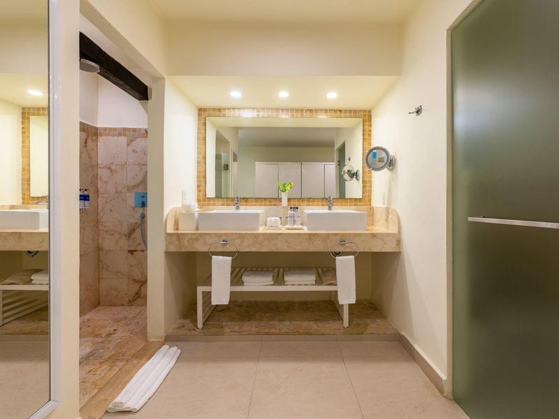 Bagno dell'hotel luminoso con doppi lavandini, grande specchio e doccia a filo pavimento.