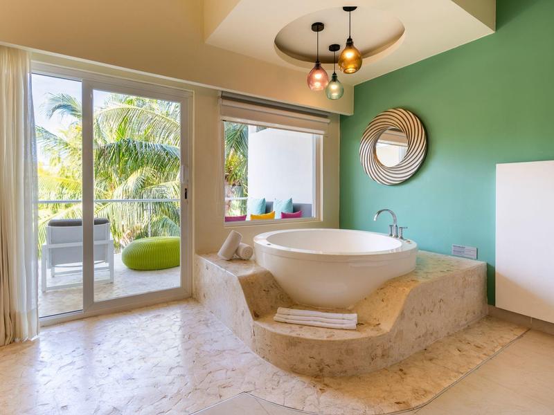 Vasca da bagno moderna in un bagno luminoso con accesso a una terrazza e parete verde.