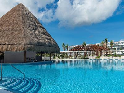 Large pool with clear blue water, thatched roof pool bar and lounge chairs.