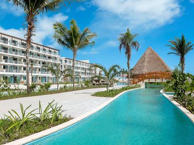 Modern hotel complex with pool and tropical palm trees under a blue sky.