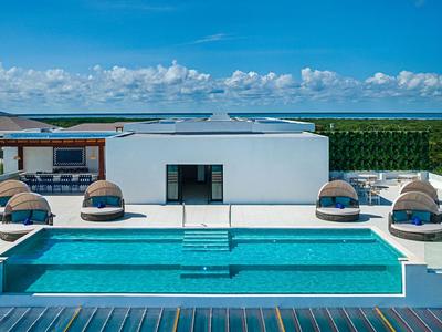 Modern hotel pool with comfortable loungers and a view of greenery and sea.