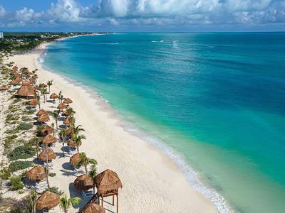 Long sandy beach with turquoise water and palm huts along the coast.