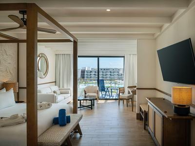 Modern hotel room with double bed, seating area, and balcony overlooking nearby buildings.