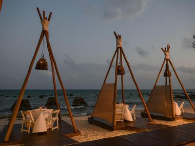 Tři jídelní prostory s dřevěnou konstrukcí na pláži při západu slunce.