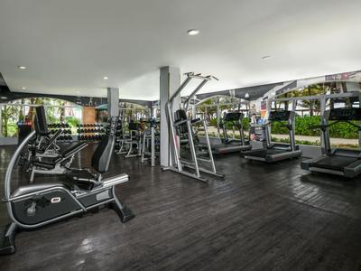 Moderní posilovna s různými tréninkovými stroji a velkými okny s výhledem na zahradu.