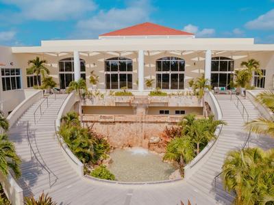 Luxusní hotel se symetrickou mostní cestou a tropickou vegetací pod modrou oblohou.