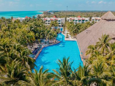 Velký bazén se skluzavkou obklopený palmami a hotelovými budovami u pláže.