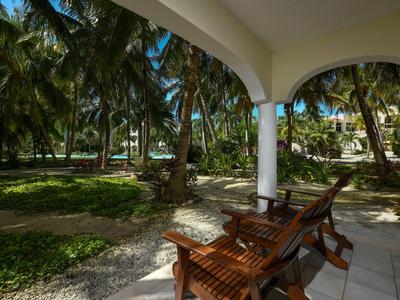 Dva dřevěné židle na kryté terase s výhledem na tropickou krajinu s palmami.