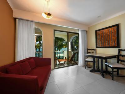 Pohled na hotelový pokoj s červenou pohovkou, stolem, židlemi a dveřmi na balkón