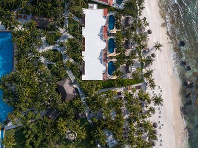 Luchtfoto van een resort met zwembad, omringd door palmbomen, direct aan het zandstrand met zeezicht.