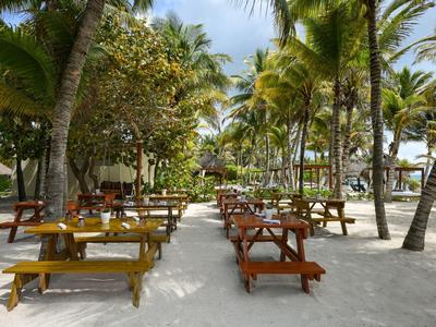 Písčitá oblast s několika dřevěnými stoly a lavicemi pod palmami u plážového hotelu.