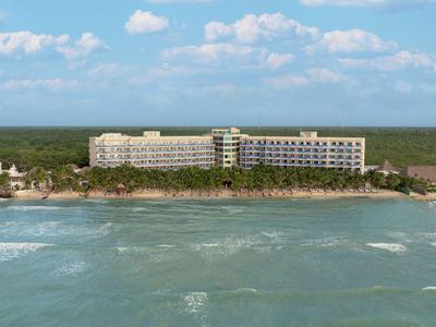 Vista di un lungo edificio dell'hotel sulla spiaggia con il mare in primo piano e il cielo azzurro.