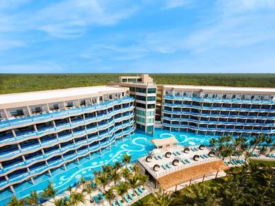 Hotel con grande piscina all'aperto circondato da vegetazione tropicale sotto un cielo blu.