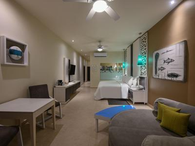 Camera d'hotel moderna con zona salotto, tavolo da pranzo e letto, illuminazione calda.