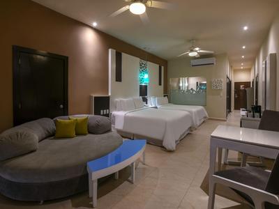 Camera d'hotel accogliente con due letti matrimoniali, divano e scrivania con illuminazione calda.