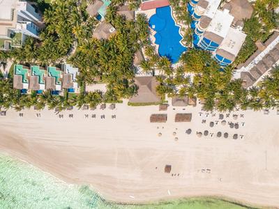 Vista aerea di una spiaggia con sedie a sdraio, piscine e vegetazione verde lungo la costa.
