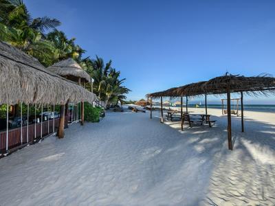 Spiaggia di sabbia bianca con palme e tetti di paglia lungo una costa tranquilla sotto un cielo limpido.