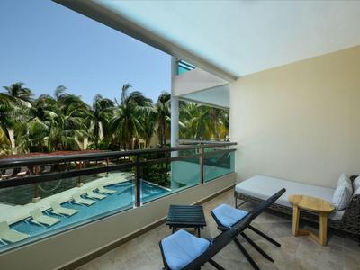 Balcone con sdraio, tavolo e vista su una piscina con palme sullo sfondo.