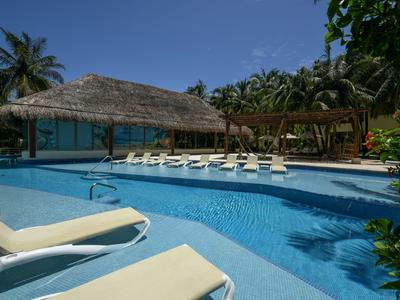 Area piscina di un hotel con lettini, tetto in paglia e vegetazione tropicale sotto un cielo limpido.