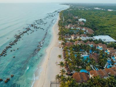 Vista aerea di un hotel sulla spiaggia con palme e mare blu.