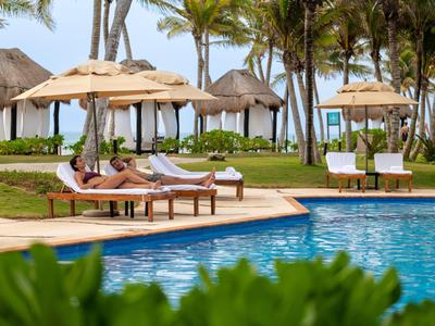 Piscina con lettini e palme in resort tropicale con tempo soleggiato.