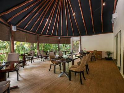 Überdachte Terrasse mit Holztischen und Stühlen, umgeben von Grünflächen.