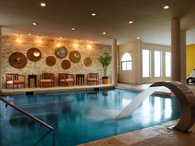 Piscina coperta con doccia a cascata, area salotto e parete decorativa con cesti.