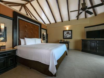 Camera d'hotel moderna con grande letto, ventilatore a soffitto e mobili in legno scuro.