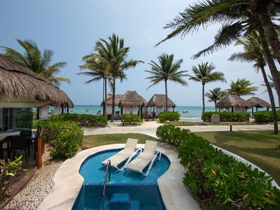 Vista di una piscina con lettini, palme e capanne sulla spiaggia vicino al mare.