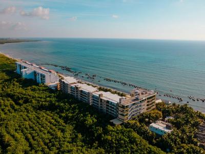 Vista aerea di un complesso alberghiero sulla spiaggia con foresta adiacente e oceano sullo sfondo.