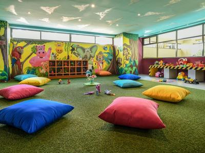 Sala giochi colorata per bambini con moquette, cuscini e murales sulle pareti.