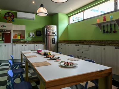 Sala da pranzo con pareti verdi, tavoli lunghi, sedie blu e grandi finestre