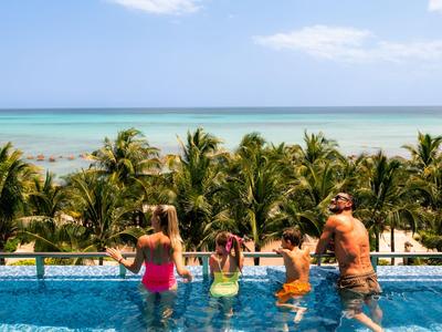 Famiglia con bambini in piscina con vista su palme e mare in una giornata di sole.