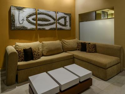 Angolo salotto accogliente con divano ad angolo marrone, tre tavoli bianchi e arte astratta da parete.