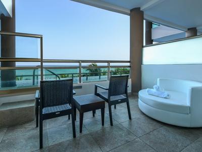 Balcone con vista mare, due sedie, tavolo e un divano bianco in una camera d'hotel.