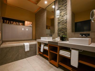 Bagno moderno con vasca, due lavabi e mensole in legno sotto uno specchio illuminato.