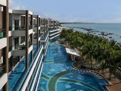 Complesso alberghiero moderno con piscina lunga e palme lungo la costa sotto un cielo sereno.